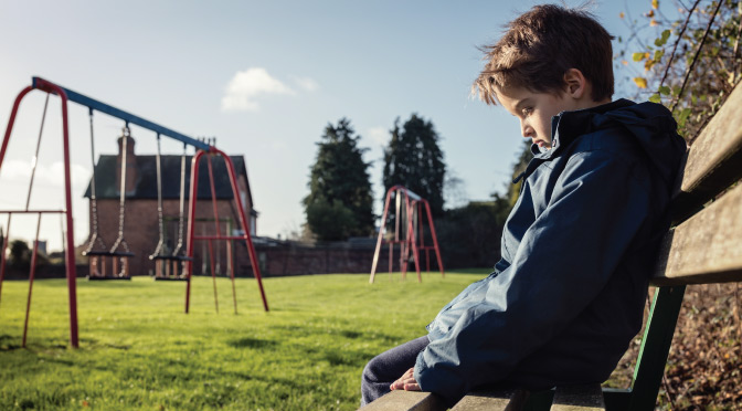 A solitary boy sitting on a bench with no supervision.